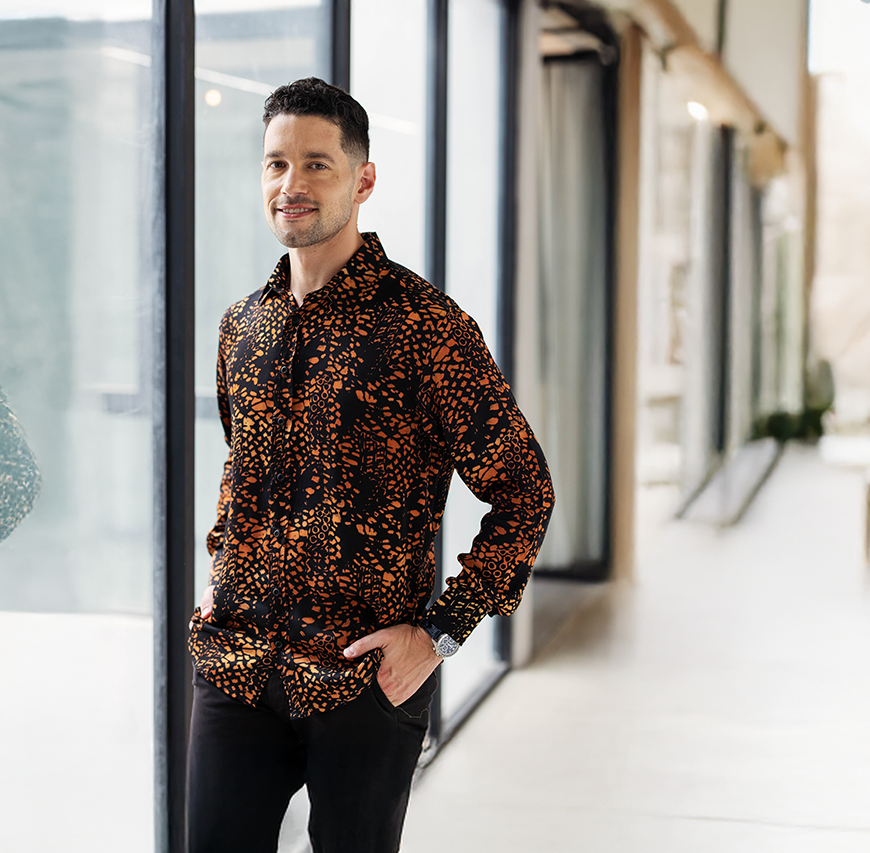 Man wearing Batik Boutique’s Black Leopard Batik Silk Shirt styled with black trousers, photographed in a modern minimalist setting. Handcrafted batik design with earthy beige tones on deep black silk for an elegant look