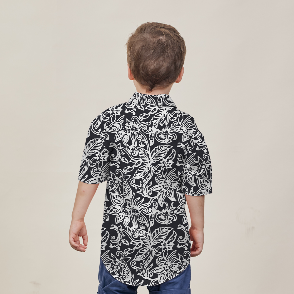 a young model posing with his back turned away from the camera while wearing a black batik shirt in the pattern black floret against a neutral background