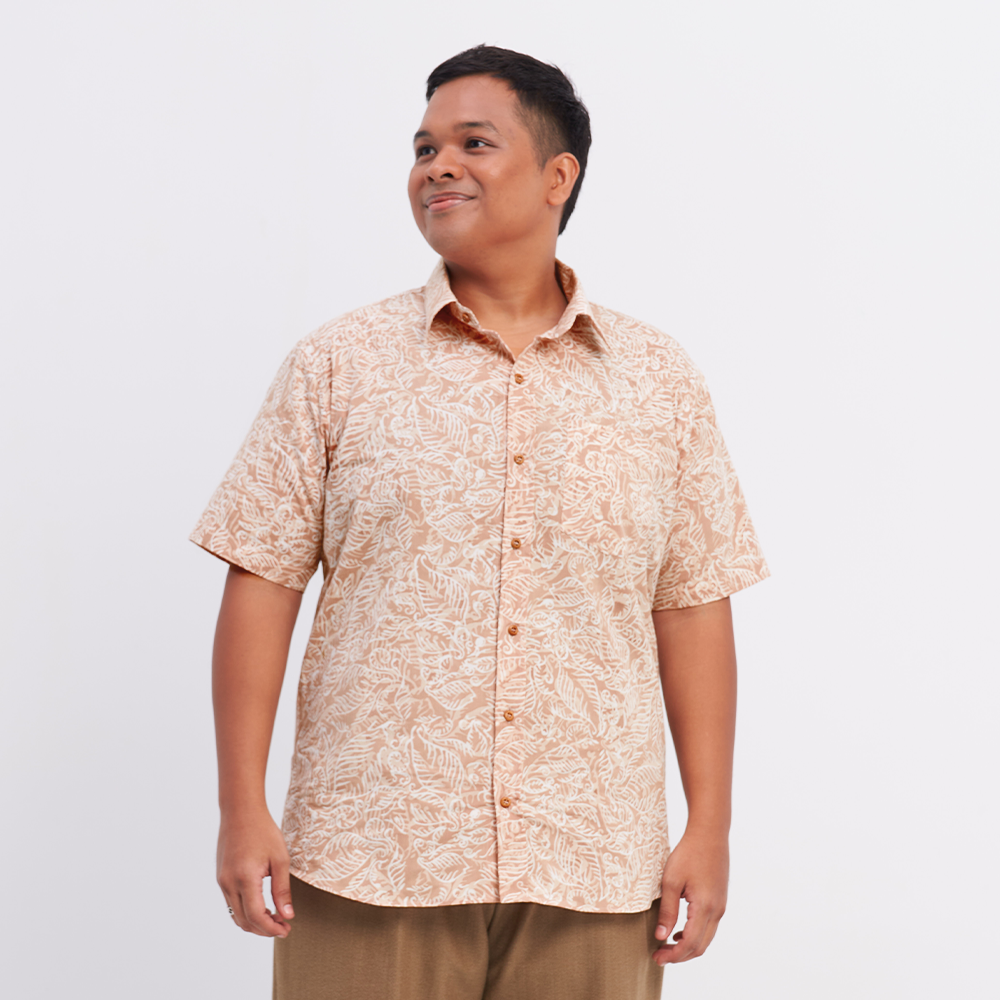 A male model posing against a white background to showcase the authentic batik shirt in the pattern tan nautical fern