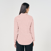 a model posing with her back to the camera while posing against a neutral background in a peach bloom shirt