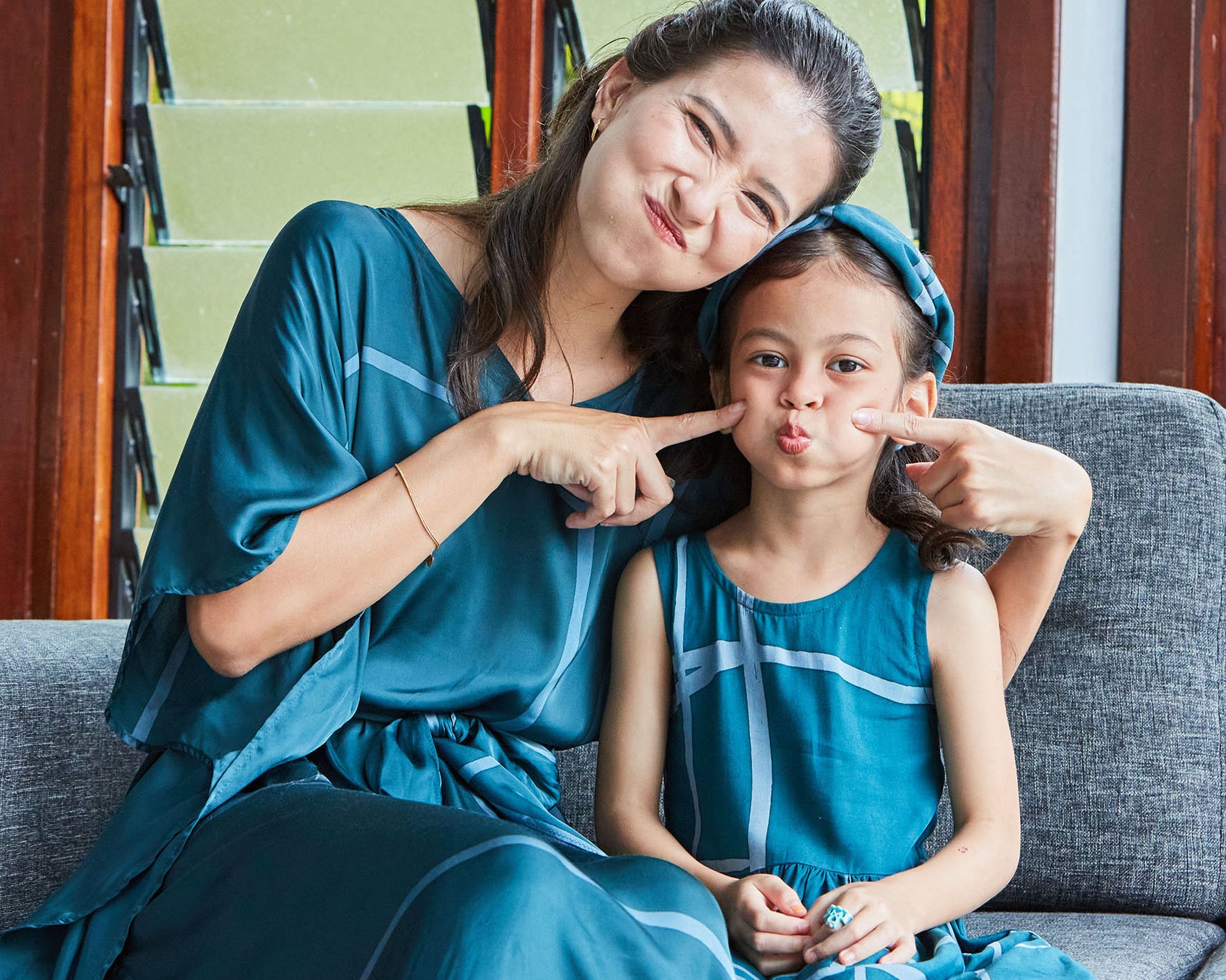 Mother and daughter sitting on sofa together dressed in matching batik dresses