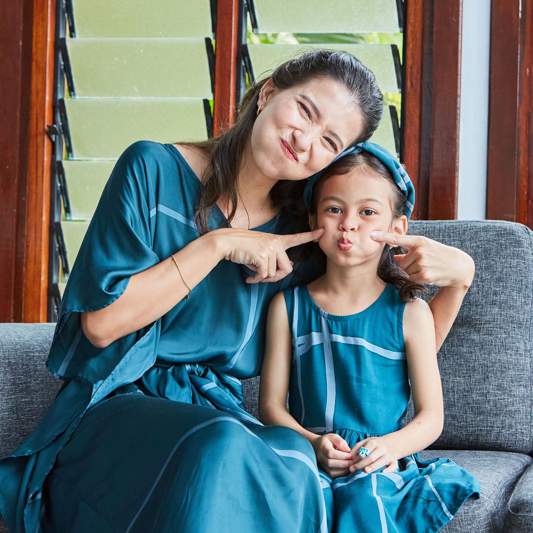 Mother and daughter sitting on sofa together dressed in matching batik dresses