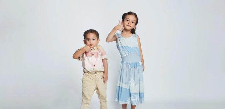 Pair of kids wearing pastel colour of apparels standing in front of white background. One is in dress of Sky Bukit another one is wearing boy shirt in Dawn Bukit. 