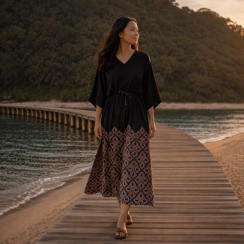 Woman in a black top and patterned skirt walking on a wooden dock by a body of water.