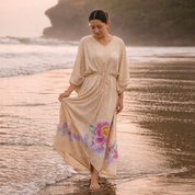 Woman in a long, light-colored dress with floral patterns walking on a beach.