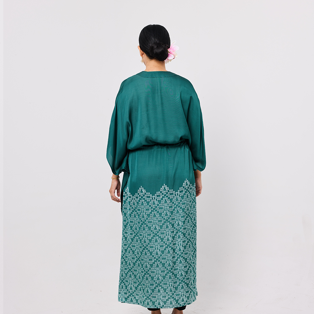 Woman wearing a teal dress with white lace details on a plain background