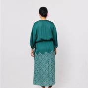 Woman wearing a teal dress with white lace details on a plain background