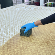 Hand wearing a blue glove holding a green sponge over a patterned surface