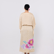 Woman wearing a beige dress with floral designs on a plain background