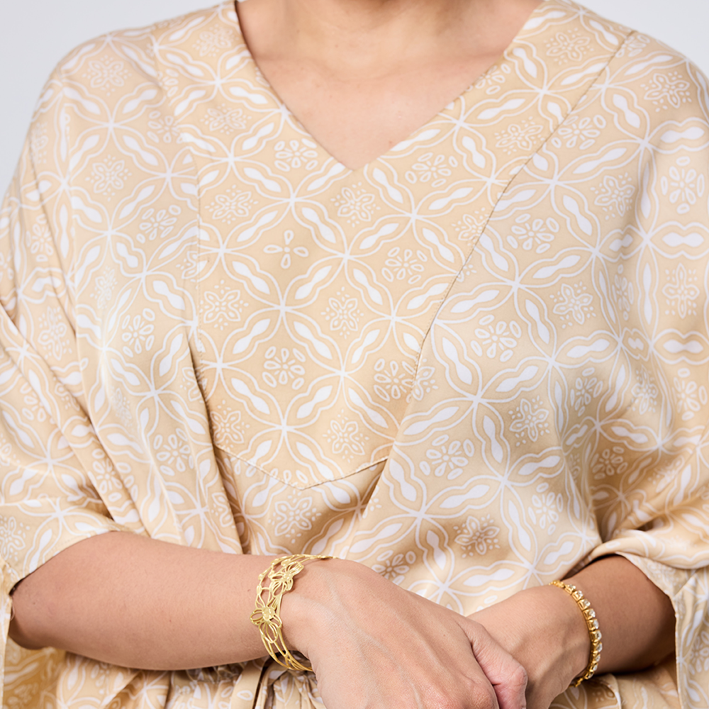 Beige patterned top worn by a person, with gold bracelets on wrists.
