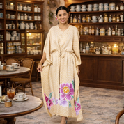 Woman in a beige dress with floral designs standing in a cozy café.