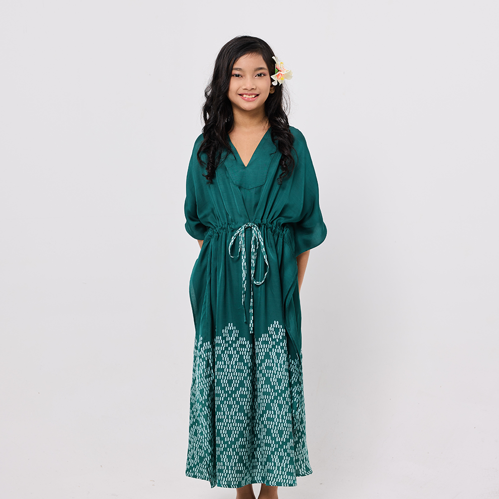 Girl wearing a green dress with a white pattern on a plain background