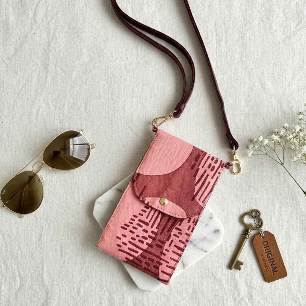 Pink patterned crossbody bag with sunglasses and a key on a light background