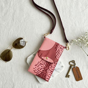 Pink patterned crossbody bag with sunglasses and a key on a light background