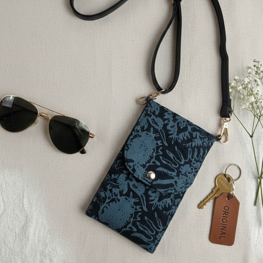Blue patterned pouch with a strap, sunglasses, and keys on a light surface.