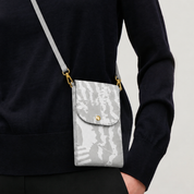 A person wearing a black sweater carries a small gray crossbody phone pouch with a gray abstract pattern, gold hardware, and a gold snap button.