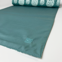 a closeup photo of a table runner in the pattern turquoise pineapple showcasing the embroidered logo
