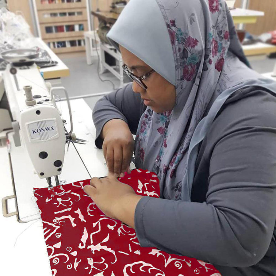 A skilled seamstress meticulously sewing an authentic batik shirt adorned with the exquisite Crimson Diwanie pattern, showcasing the craftsmanship in progress
