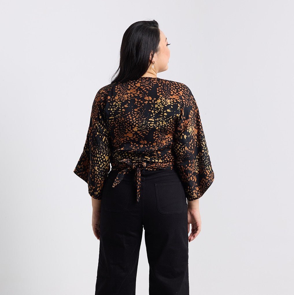 Woman wearing a patterned top and black pants on a plain background