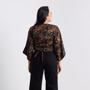 Woman wearing a patterned top and black pants on a plain background