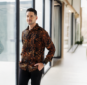 Man wearing Batik Boutique’s Black Leopard Batik Silk Shirt styled with black trousers, photographed in a modern minimalist setting. Handcrafted batik design with earthy beige tones on deep black silk for an elegant look