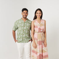 a man standing in front of white background styling batik cuban shirt in olive pineapple pattern  & a woman wearing maxi dress in dawn bukit pattern