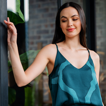 A model exuding elegance in a lifestyle photo, donning a Forest Chain patterned batik camisole while leaning against a window