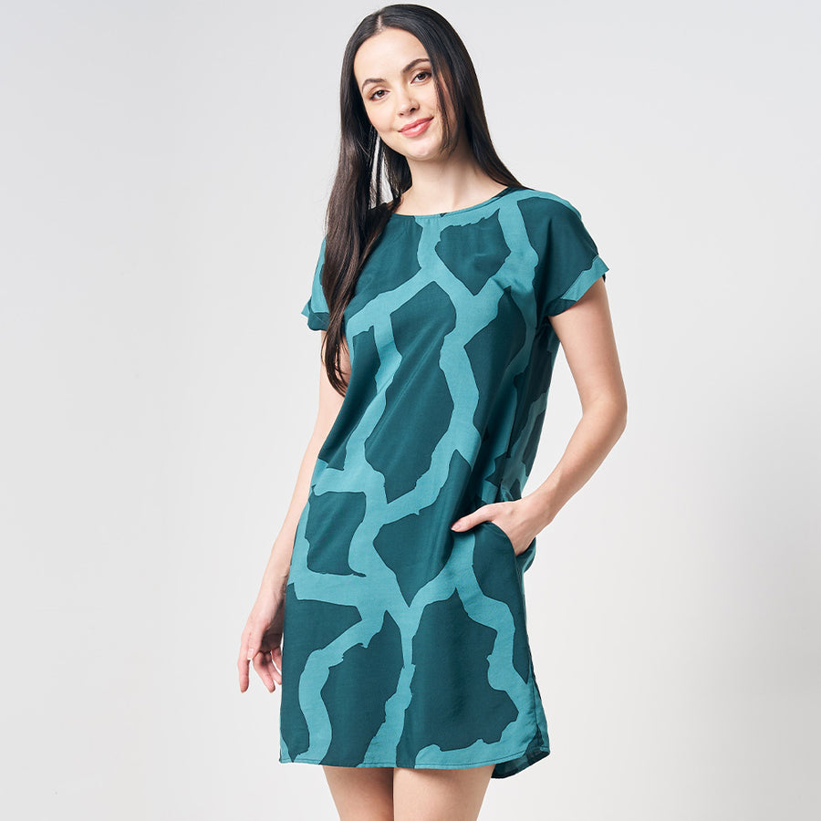 A woman gracefully posing in front of a white background, adorned in a batik dress featuring the Forest Chain pattern, showcasing the stylish and timeless design