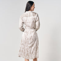 A woman elegantly donning a long shirt dress crafted using the Shibori technique, presented against a neutral background, showcasing the unique and stylish design