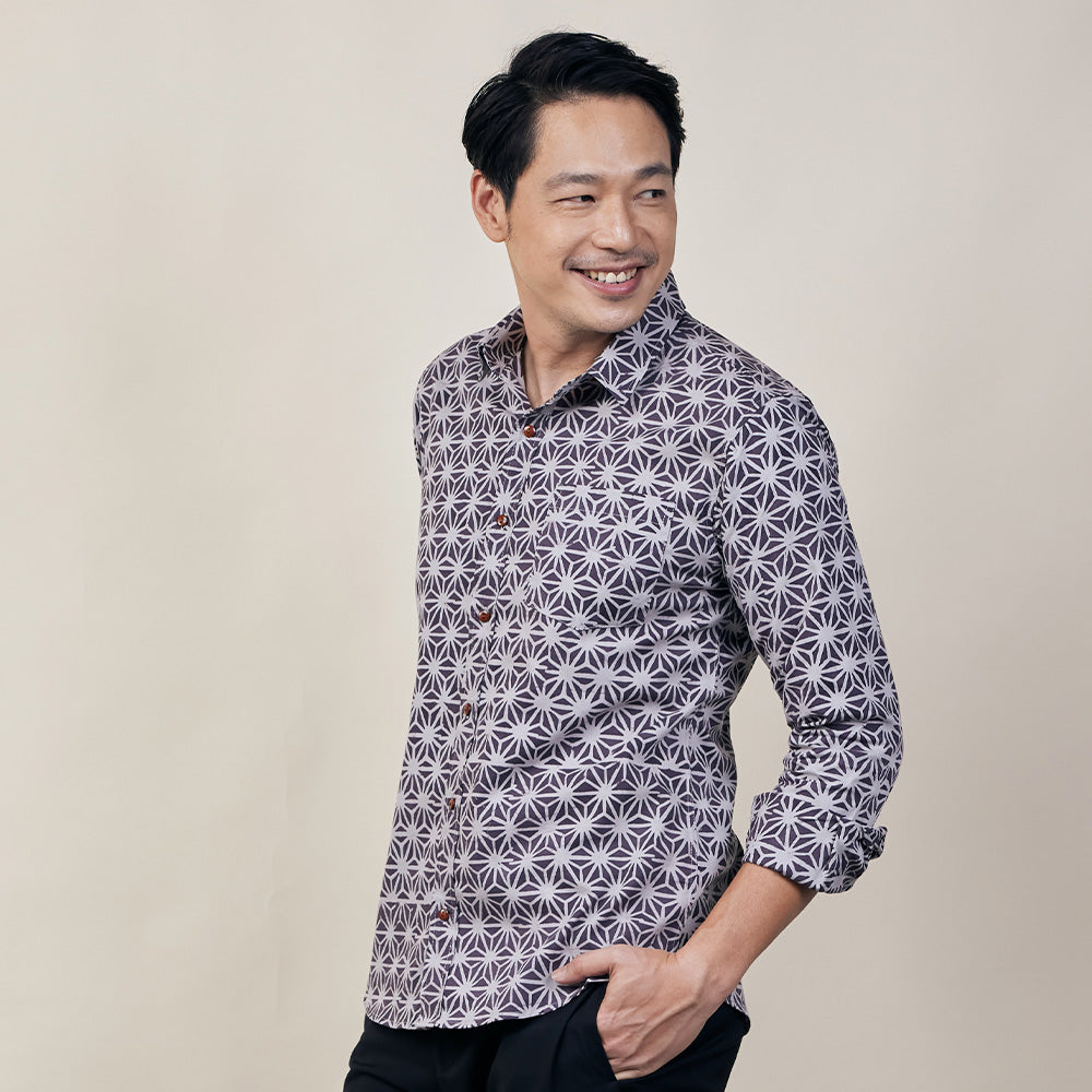 A man in purple batik long sleeved shirt standing in front of beige background