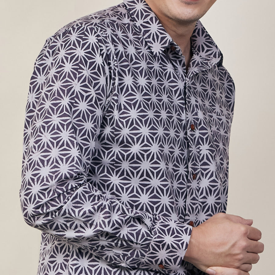 A close up photo of man in purple batik long sleeved shirt standing in front of beige background