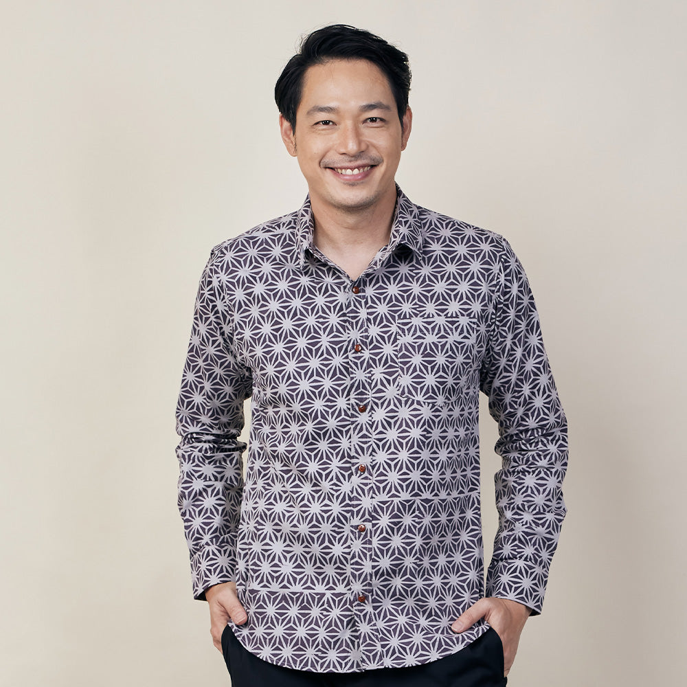 A man in purple batik long sleeved shirt standing in front of beige background