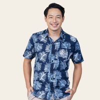 a picture of a male model posing in front of a neutral background while smiling happily while wearing a batik shirt in the pattern navy sawit
