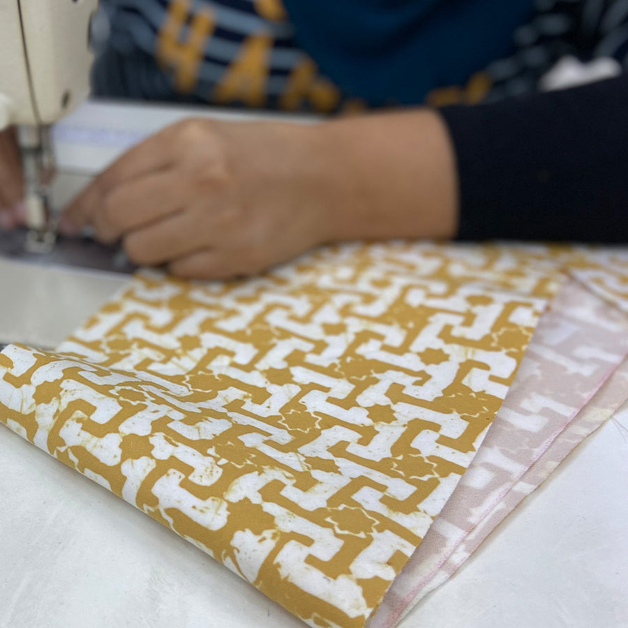 a seamstress in the process of sewing mustard arabesque patterned batik