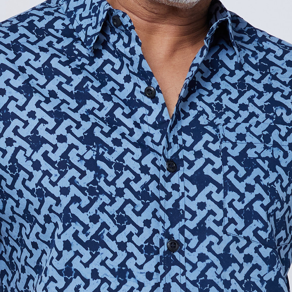 A closeup of a man wearing blue batik shirt in midnight arabesque pattern standing in front of white backrgound