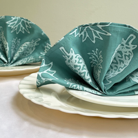a lifestyle photo of batik serviettes on top of a stack of plates against a neutral background
