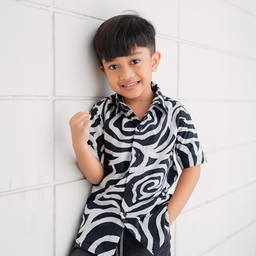 a small boy posing in a batik shirt in the pattern black kerepek in a lifestyle photo