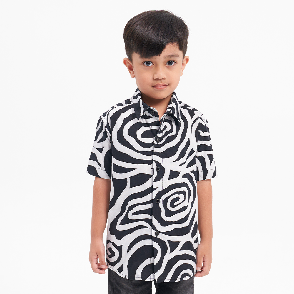 a whitebox photo of a small boy in a batik shirt in the pattern black kerepek