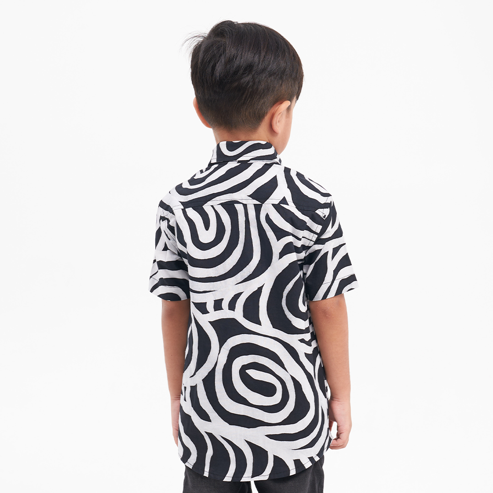 a back of a boy posing in a batik shirt in the pattern black kerepek against a white background