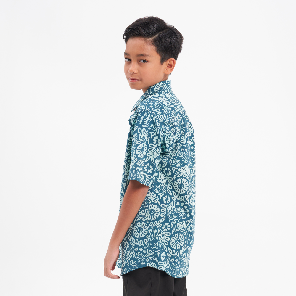 a boy model posing in a batik shirt in the pattern teal ukir against a white background