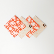 Artisan-crafted peach batik coasters with starburst pattern, set of four coasters, Square cotton coasters featuring peach firework batik design, reversible sides in matching tones, handcrafted by Malaysian artisans. Peach and white batik coasters in starburst motif, reversible fabric with Batik Boutique logo box, ideal for home décor or gifting. Perfect for  drinking, parties, Events
Stocking stuffer. Fabric coasters. Batik Boutique 