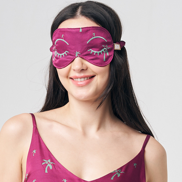 a model happily posing in an eye mask made of authentic batik in the pattern fuchsia palm against a white background