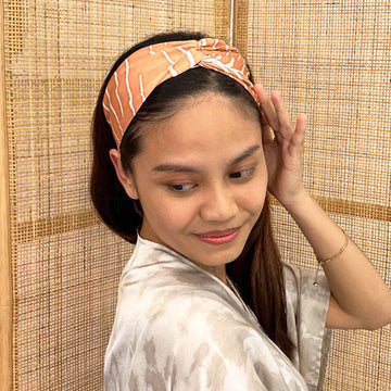 A model is wearing batik headband in peach fern print. Made from batik remnant fabric