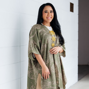 A woman wearing a moss green batik kimono with an orchid motif, smiling against a white wall