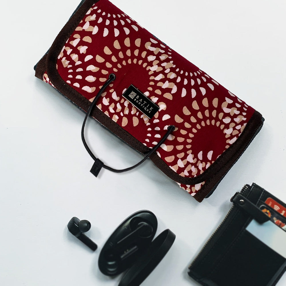 Lifestyle photo of a handmade batik roll-up travel pouch in the Crimson Lunar pattern, featuring a secure string closure.