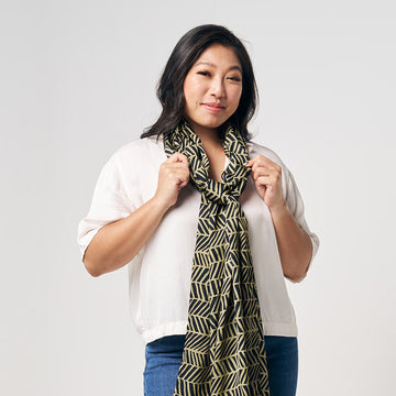 A women is styling batik block scarf in black banana leaf while standing in front of white background