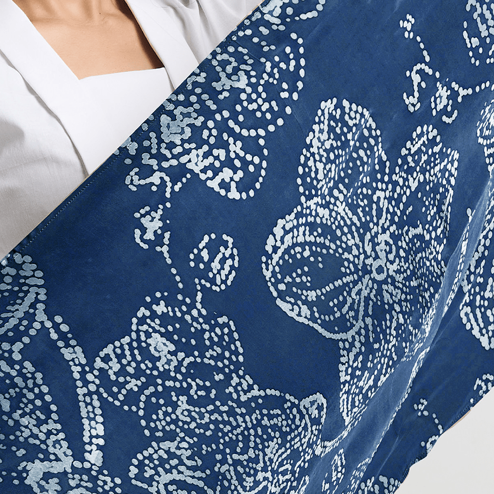 A close-up of the navy-blue batik scarf with an orchid print, showing the detailed floral design with a soft sheen of the silk cotton fabric.
