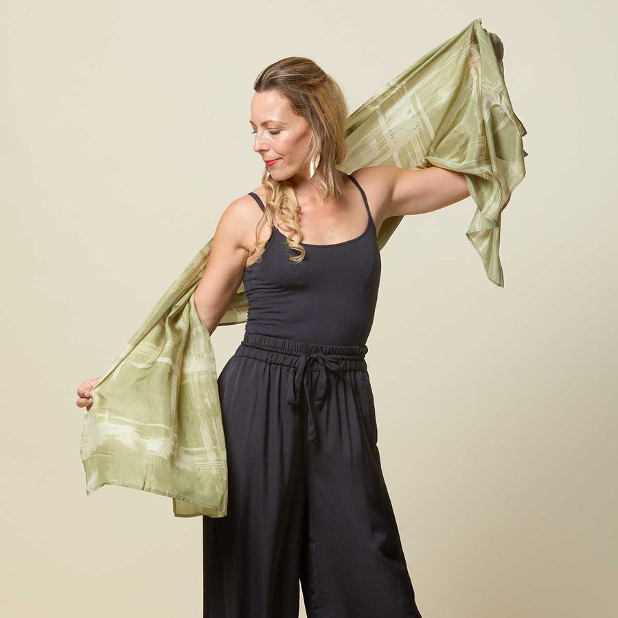Woman playing around with long batik scarf in olive cotton silk.