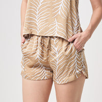 A women is wearing hand-crafted and hand-painted batik PJ shorts in Latte Fern pattern. The model is putting hand in pocket while standing in front of white background