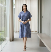 Woman wearing a blue dress standing in a modern indoor setting with large windows.